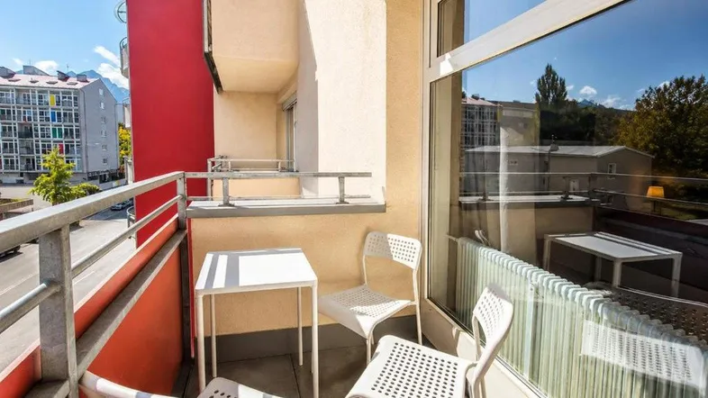Heller Balkon mit weißem Tisch und Stühlen, bietet einen Blick auf die umliegenden Gebäude.