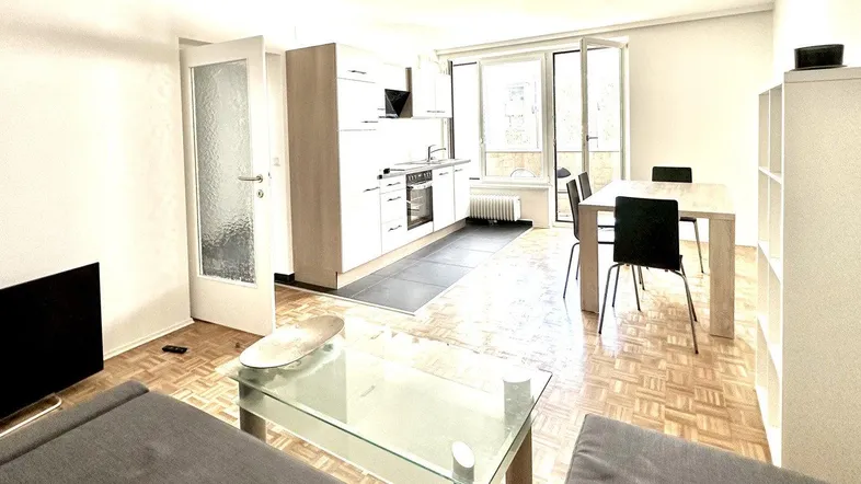 Heller offener Wohn- und Essbereich mit integrierter Küche, Parkettboden und Zugang zum Balkon.