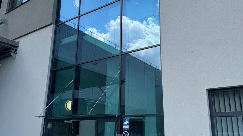 Moderner Gebäudeeingang mit großer Glasfassade, die den Himmel und Wolken widerspiegelt.