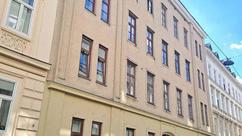Mehrstöckiges Wohngebäude mit klassischer Fassade und parkenden Autos auf der Straße.