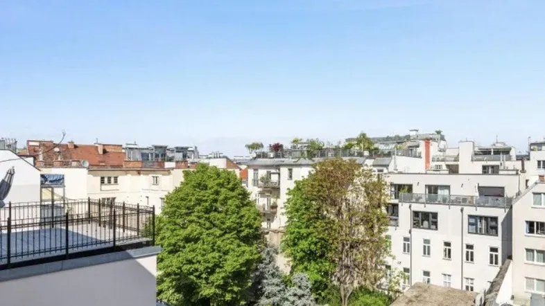 Blick über die Dächer der Stadt mit grünen Bäumen und einem ruhigen Innenhof unter blauem Himmel.