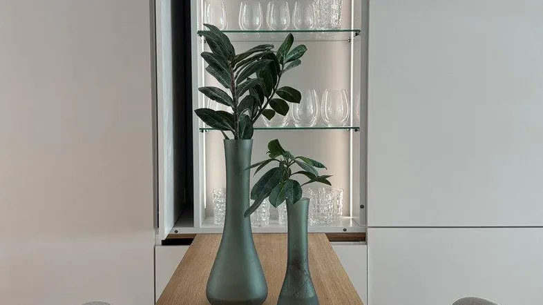 Moderne Küchenzeile mit Holztresen, Barhockern und beleuchtetem Glasregal für Geschirr.