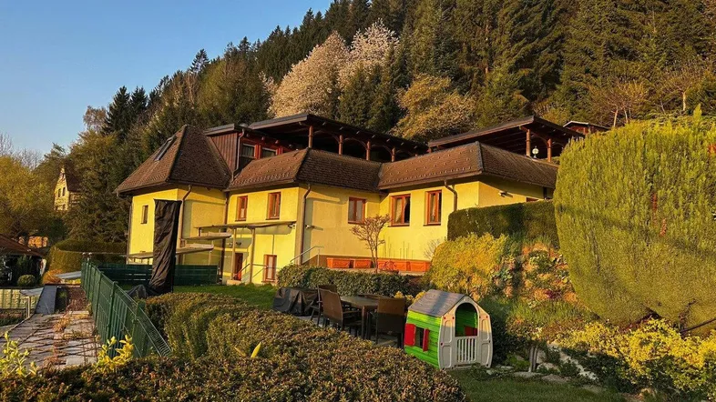 Großzügiger Gartenbereich mit Sitzgelegenheiten und Spielhaus, umgeben von grüner Natur und Wald.