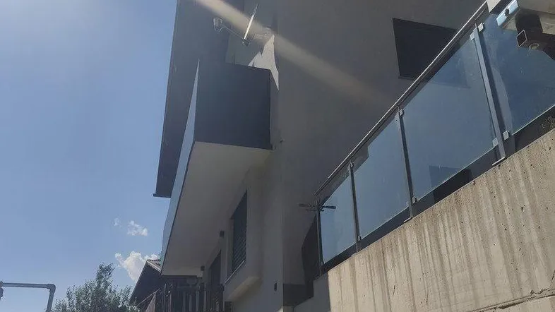 Moderne Gebäudefassade mit Balkonen und einem Teil des Gartens unter strahlendem Sonnenschein.