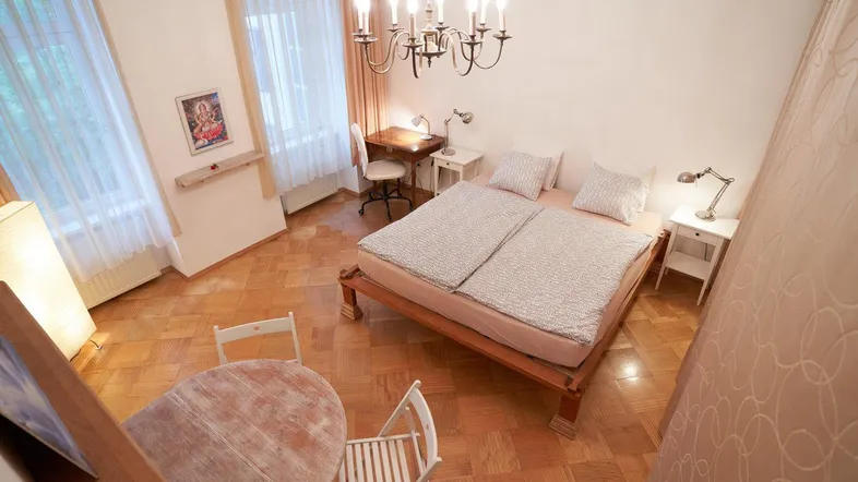 Helles Schlafzimmer mit Parkettboden, Doppelbett, Schreibtisch und einem kleinen Essbereich.