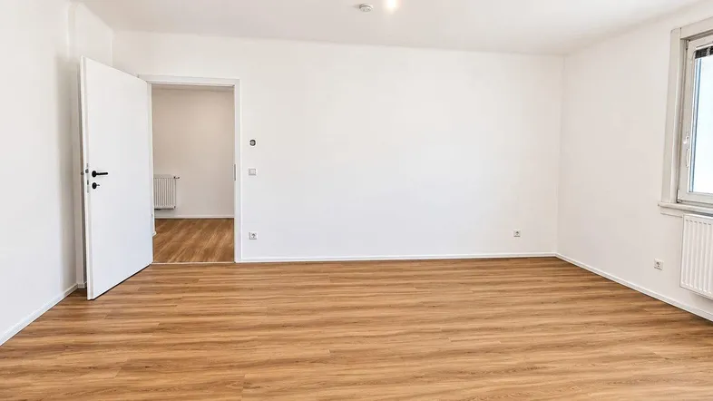 Helles, leeres Zimmer mit Laminatboden und weiß gestrichenen Wänden, bereit zur individuellen Gestaltung.