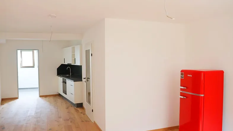 Helle offene Wohnküche mit Holzboden und einem auffälligen roten Kühlschrank.