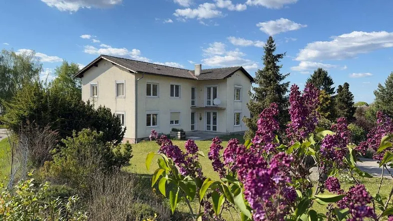 Helles Haus mit gepflegtem Garten und blühenden Sträuchern unter blauem Himmel.