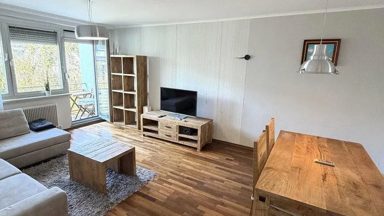 Helles Wohn- und Esszimmer mit Holzboden, bequemer Couch und Zugang zum Balkon.