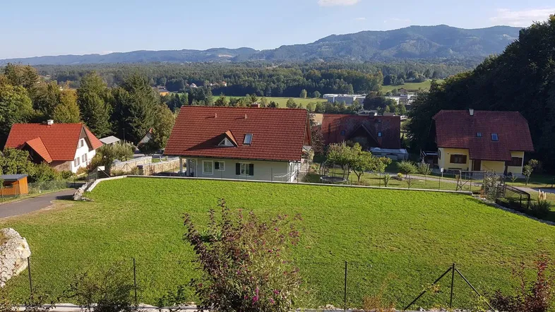 Panoramablick auf mehrere Häuser in ländlicher Umgebung mit grünen Wiesen und bewaldeten Hügeln im Hintergrund.