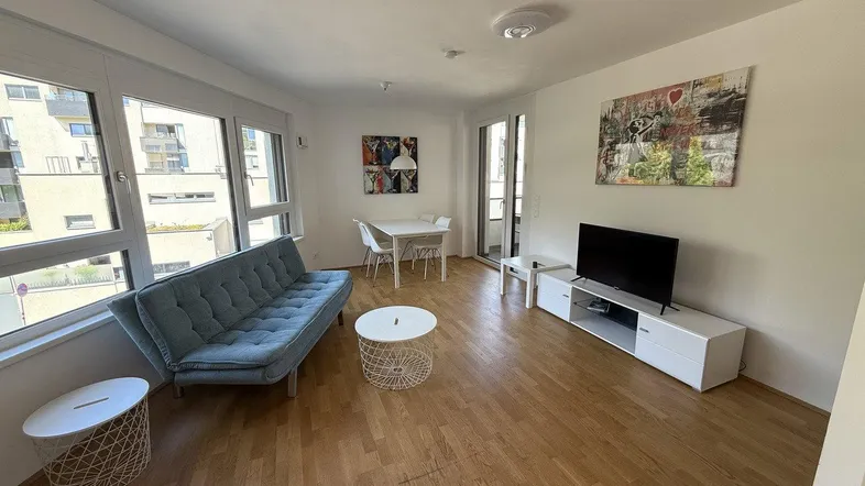 Helles Wohn- und Esszimmer mit Parkettboden, bequemer Couch und Zugang zum Balkon.