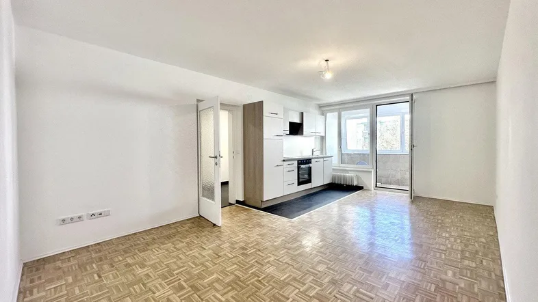 Heller Wohnbereich mit Parkettboden und integrierter Küchenzeile, bietet Zugang zu einem Balkon.