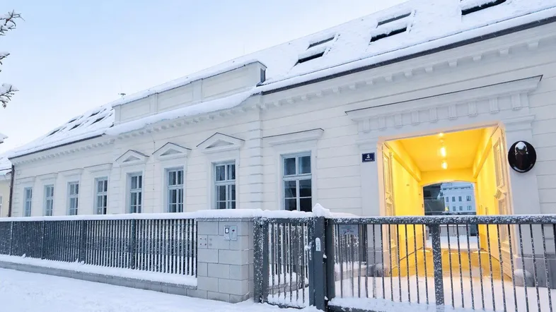 Elegante Fassade eines Gebäudes im Winter mit verschneitem Eingangsbereich und hellem Durchgang.