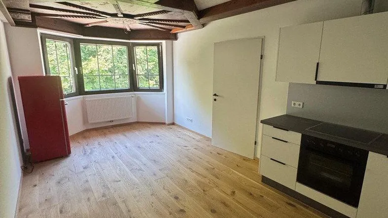 Helles Zimmer mit Holzbalkendecke, Erkerfenster und integrierter Küchenzeile, ideal als Wohn-Essbereich.