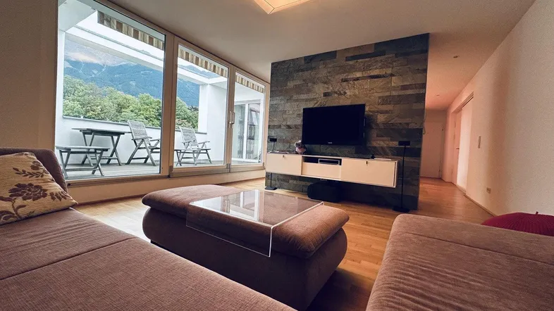 Helles Wohnzimmer mit bequemer Couch, Holzboden und Zugang zu einer Terrasse mit Bergblick.