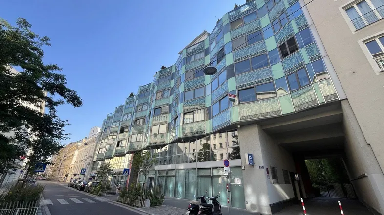 Moderne Architektur mit geschwungener Glasfassade und begrünten Dächern in urbaner Umgebung.