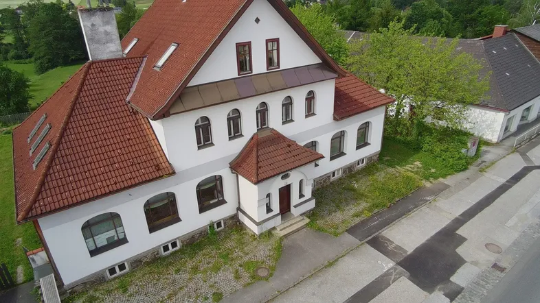 Historisches Gebäude mit weißer Fassade und rotem Ziegeldach in ländlicher Umgebung.