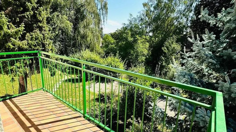Heller Balkon mit grüner Brüstung und Blick ins Grüne an einem sonnigen Tag.