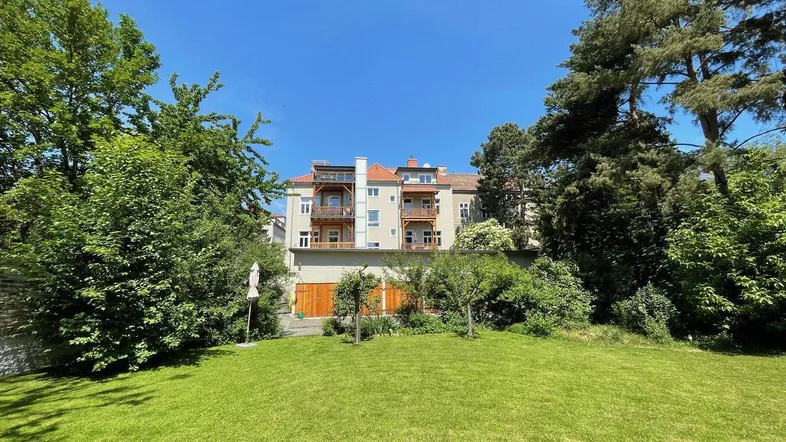 Großzügiger Gartenbereich mit Rasenfläche und Blick auf das Mehrfamilienhaus mit Balkonen.