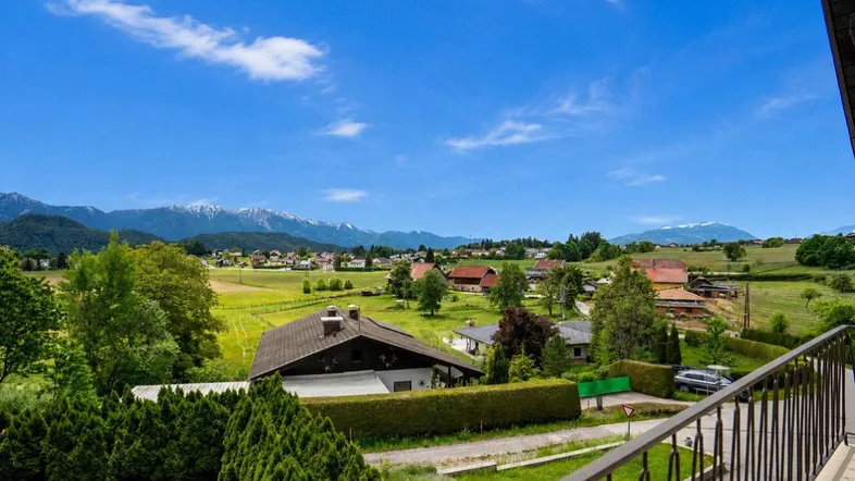 Weitläufiger Blick über grüne Landschaft mit Häusern und schneebedeckten Bergen am Horizont.