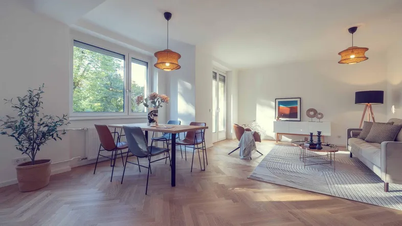 Helles Wohn- und Esszimmer mit Fischgrätparkett, modernen Möbeln und großen Fenstern mit Grünblick.