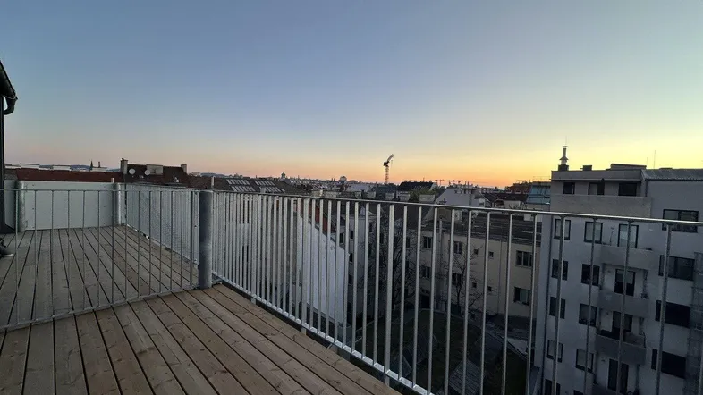 Geräumige Dachterrasse mit Holzboden und weitem Blick über die Stadt bei Sonnenuntergang.