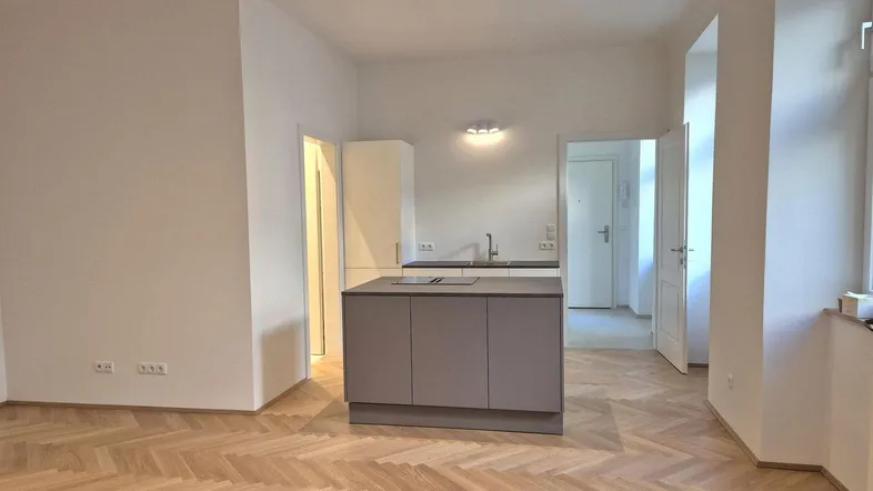 Helles, offenes Wohnzimmer mit Fischgrätparkett und moderner Kücheninsel, bereit zur Einrichtung.