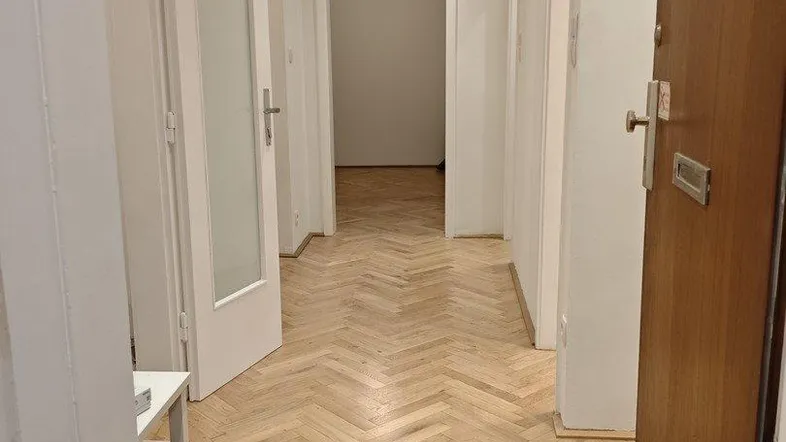 Heller Flur mit Fischgrätparkettboden, weißen Wänden und Einbaustrahlern an der Decke.