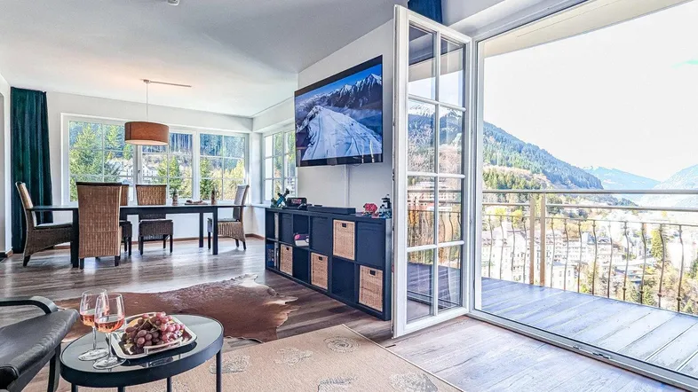 Helles Wohn- und Esszimmer mit Holzboden, Bergblick und Zugang zum Balkon.