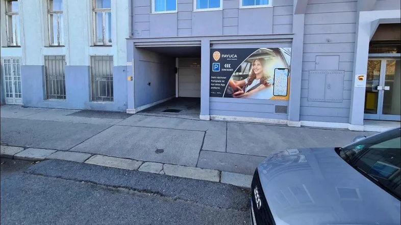 Eingang zu einer Tiefgarage mit Werbeplakat für Parkmöglichkeiten an der Fassade eines Gebäudes.