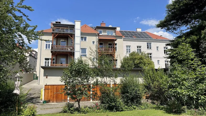 Mehrfamilienhaus mit mehreren Balkonen, Solaranlage auf dem Dach und einem gepflegten Gartenbereich.