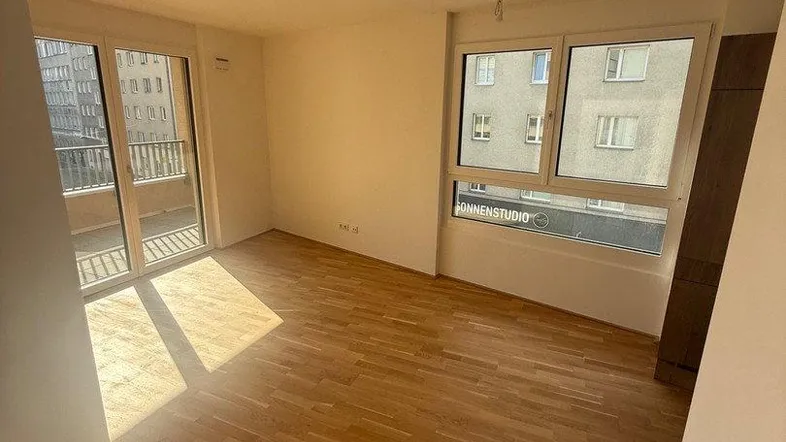 Helles Wohnzimmer mit Parkettboden, großen Fenstern und Zugang zu einem Balkon.