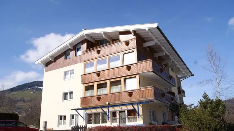 Mehrstöckiges Gebäude mit traditionellen Holzbalkonen und schneebedeckter Landschaft im Hintergrund.