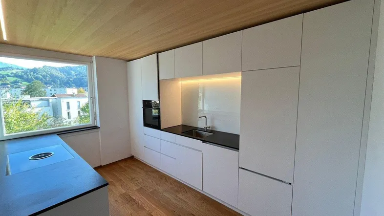 Moderne Küche mit weißen Hochglanzfronten, Holzboden und einem Fenster mit Bergblick.