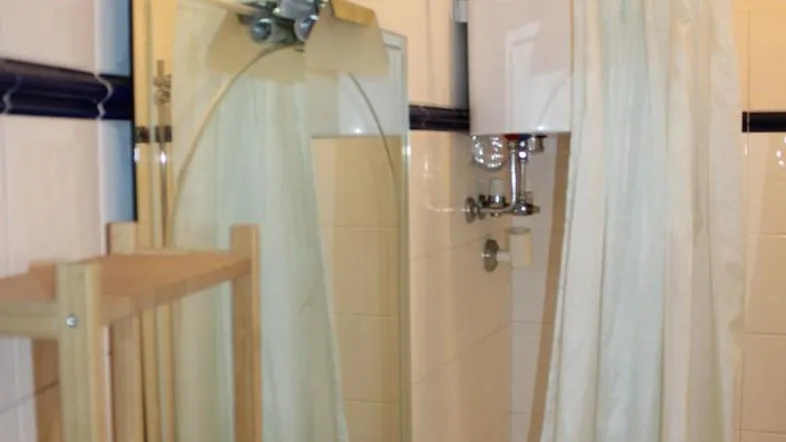 Badezimmer mit Waschbecken, Spiegel und Duschvorhang, in einem älteren Stil gehalten.