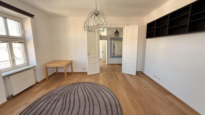 Helles Zimmer mit Parkettboden, dekorativer Deckenleuchte und Zugang zu weiteren Räumen.