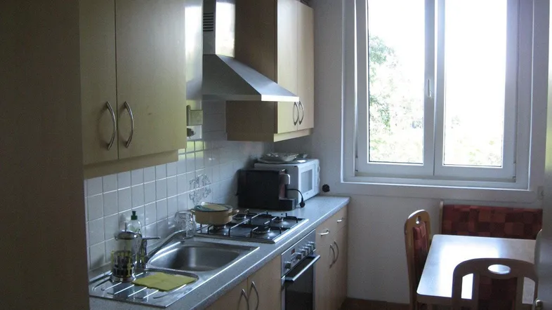 Helle Küche mit Einbaugeräten, Essbereich und Fenster mit Blick ins Grüne.