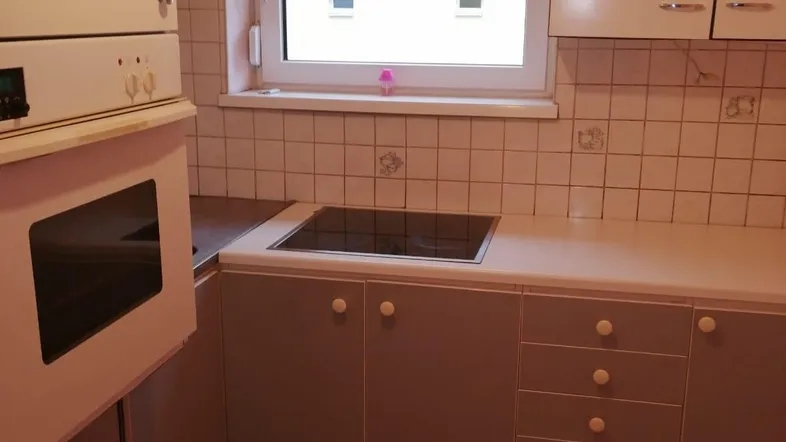 Küche mit Einbaugeräten, Fliesenboden und Fenster mit Rollladen.