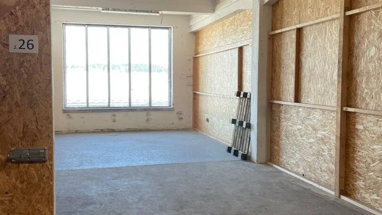 Leerer Lagerraum mit OSB-Trennwänden, Betonboden und großen Fenstern für natürliches Licht.