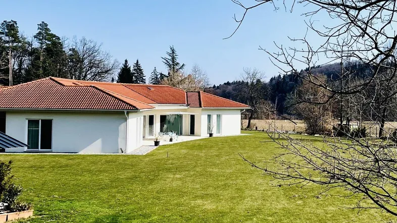 Modernes Haus mit rotem Ziegeldach und weitläufigem grünen Rasen in ländlicher Umgebung.