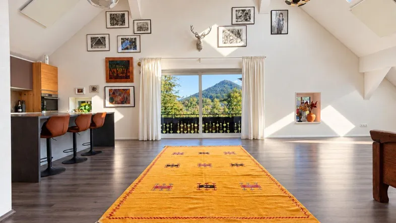 Helles Dachgeschoss-Loft mit offener Küche, Holzbalken und Bergblick vom Balkon.