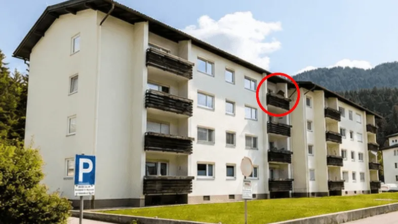 Mehrstöckiges Wohngebäude mit Balkonen und grüner Umgebung in den Bergen.