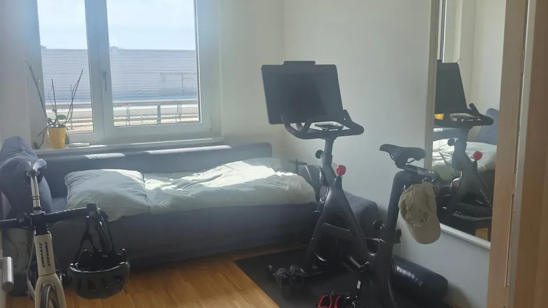 Helles Zimmer mit Bett, Sportgeräten und Fensterblick, ideal für Fitness und Entspannung.