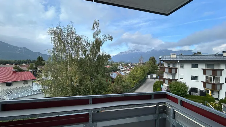 Balkon mit Bergblick und Aussicht auf die umliegende Wohngegend unter bewölktem Himmel.