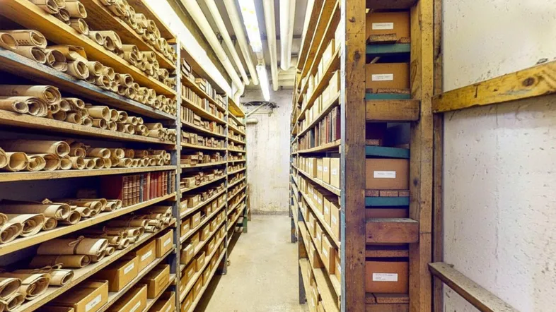 Langer Lagerraum mit hohen Holzregalen, gefüllt mit alten Schriftrollen und Archivboxen.