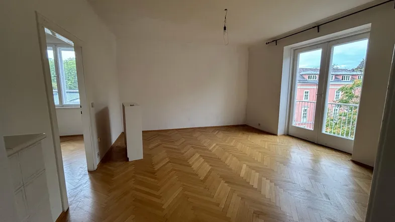 Helles Zimmer mit Fischgrätparkett und Zugang zu einem französischen Balkon, ideal als Wohn- oder Schlafzimmer.