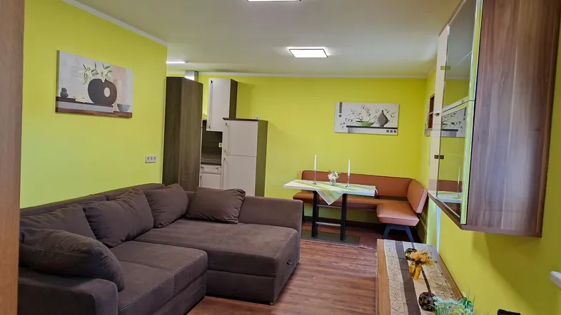 Heller Wohn- und Essbereich mit Sofa, Esstisch und integrierter Küchenzeile in lebendigem Gelb.