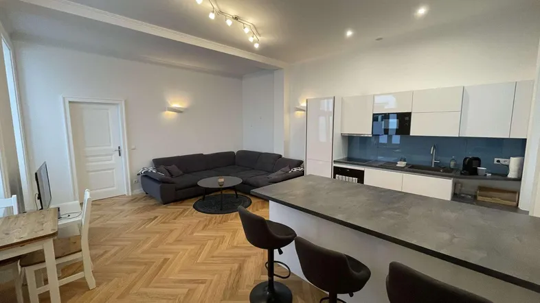 Heller offener Wohn- und Essbereich mit moderner Küche, Sofa und Fischgrätparkettboden.