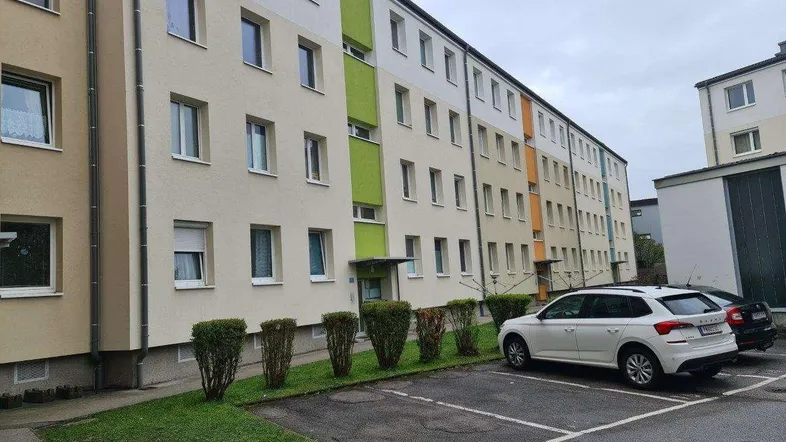 Mehrfamilienhaus mit farbiger Fassade und Parkplätzen im Freien vor dem Gebäude.