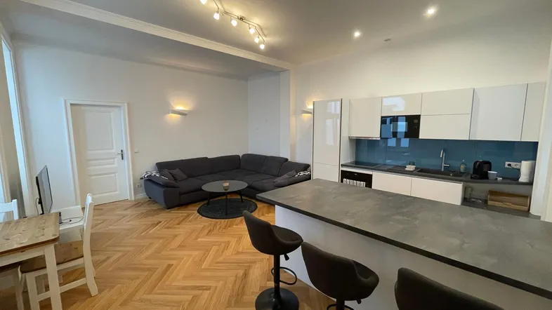 Heller, offener Wohn-Essbereich mit moderner Küche, Parkettboden und gemütlichem Sofa.